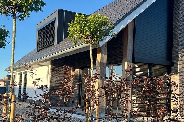 Eigentijds huis met donkere luiken en houten accenten, omringd door jonge bomen Eigentijds huis met donkere luiken en houten accenten, omringd door jonge bomen