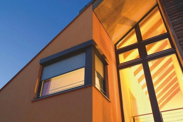 Gevel van een eigentijds huis bij avondlicht met verlichte ramen en rolluik Gevel van een eigentijds huis bij avondlicht met verlichte ramen en rolluik