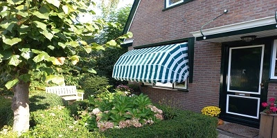 Huis met bakstenen muur, groen-witte markiezen en bloeiende tuin Huis met bakstenen muur, groen-witte markiezen en bloeiende tuin