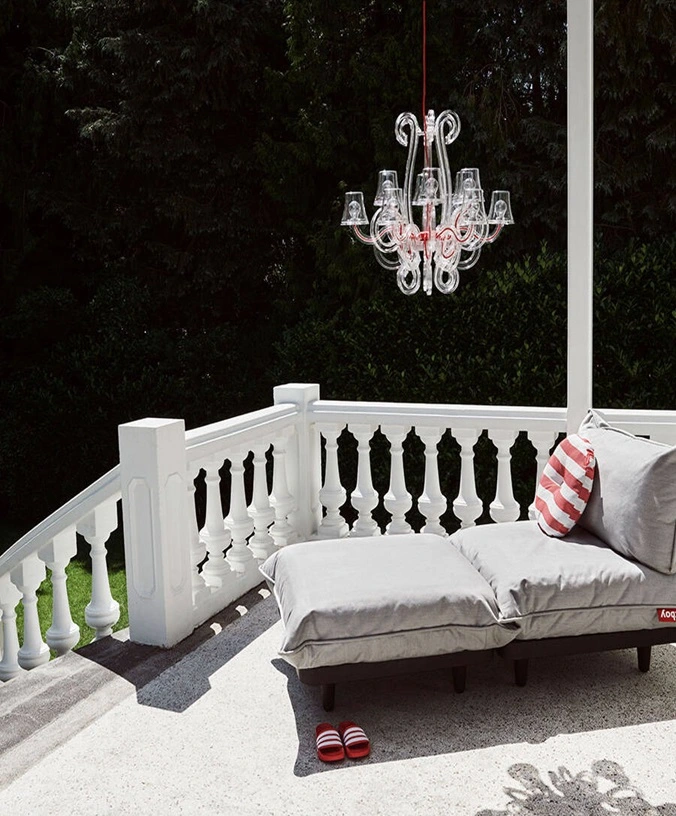 Grijze lounge bank, rood-wit gestreept kussen, en een hangende kroonluchter Grijze lounge bank, rood-wit gestreept kussen, en een hangende kroonluchter