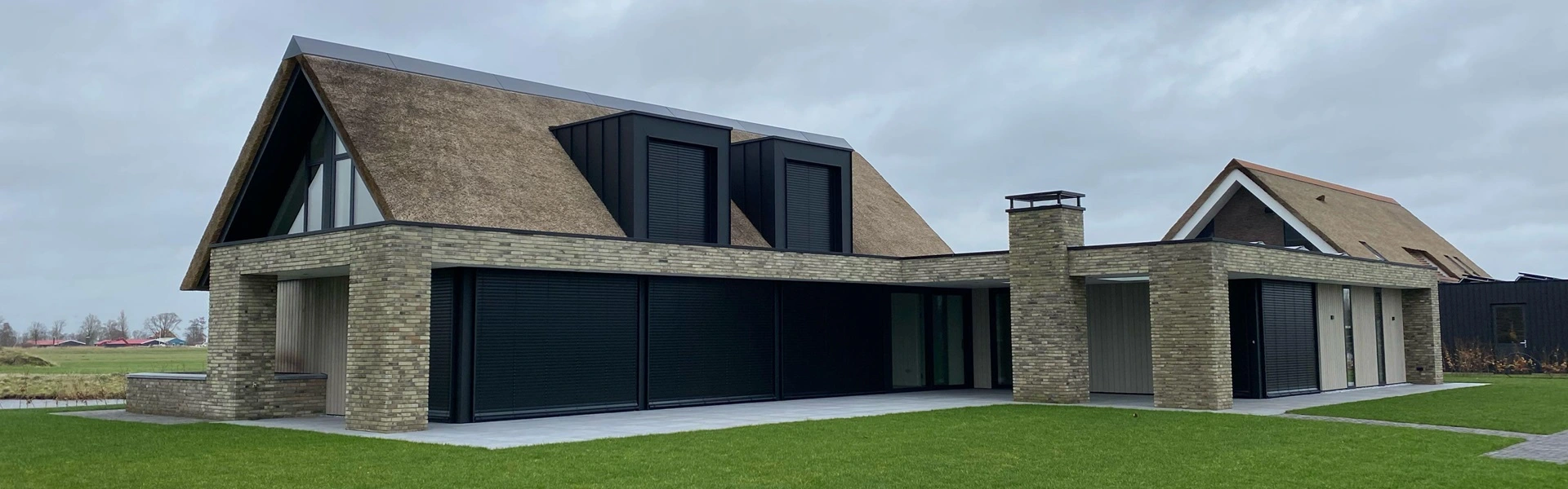 Buitenjaloezie raffstore op rieten dakwoning met groene tuin