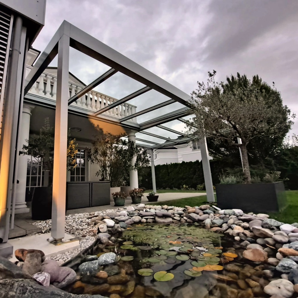 Glazen tuinkamer Cubo naast vijver met verlichting bij schemering