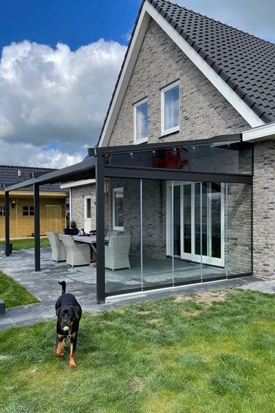 Overkapping Viva aan huis met glazen wanden en hond in tuin Overkapping Viva aan huis met glazen wanden en hond in tuin