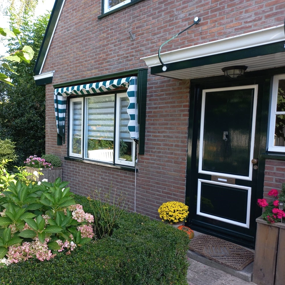 Aluminium markies met groene en witte strepen boven een raam naast de voordeur