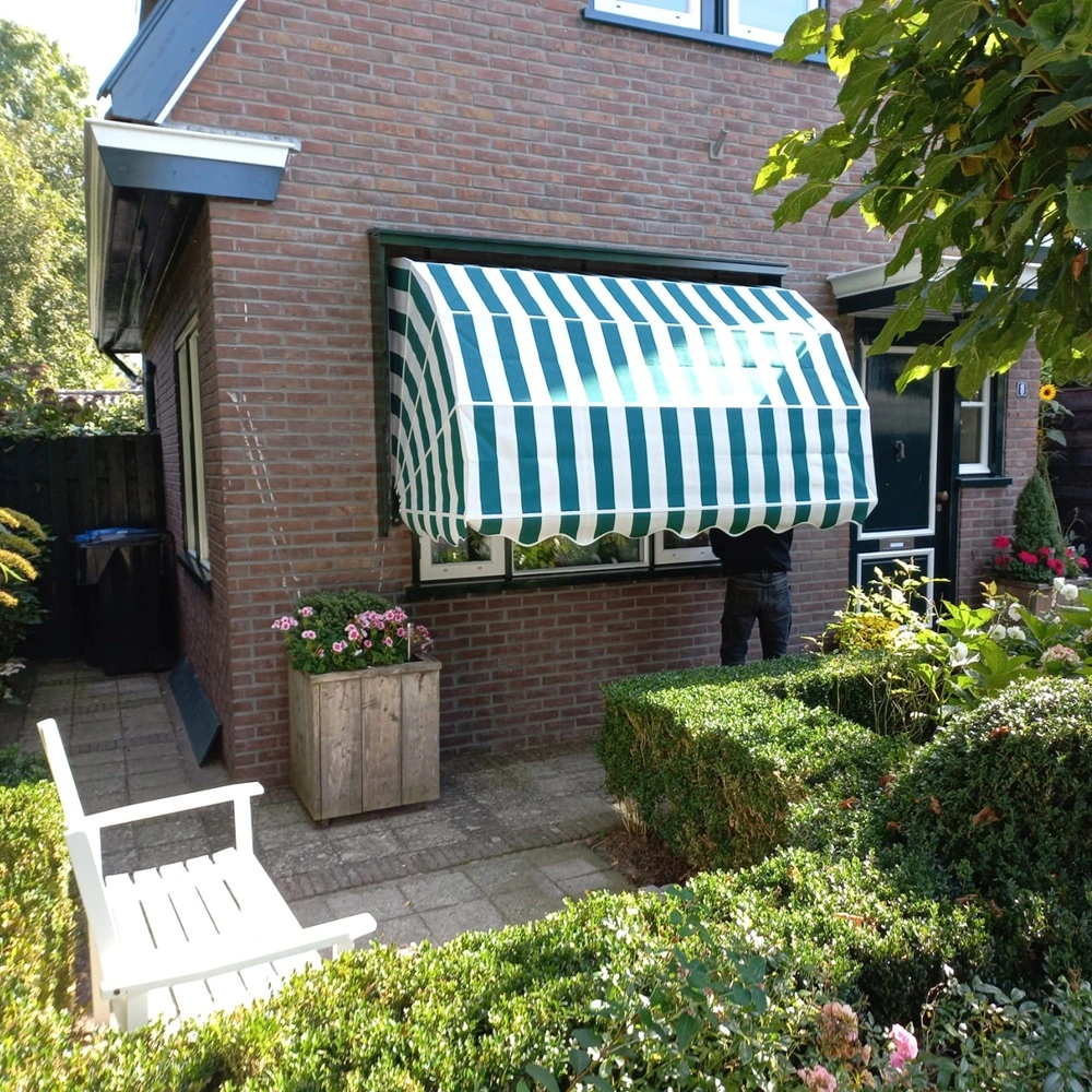 Aluminium markies met groene en witte strepen in tuin bij een woning