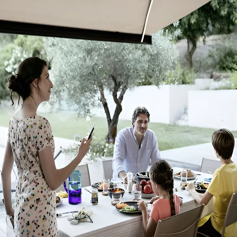 Gezin geniet van maaltijd buiten onder elektrische zonwering van Somfy Gezin geniet van maaltijd buiten onder elektrische zonwering van Somfy