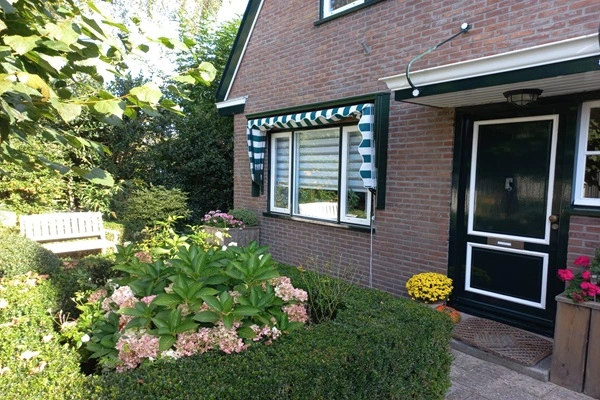 Groen-wit gestreepte markies boven raam naast voordeur van bakstenen huis Groen-wit gestreepte markies boven raam naast voordeur van bakstenen huis