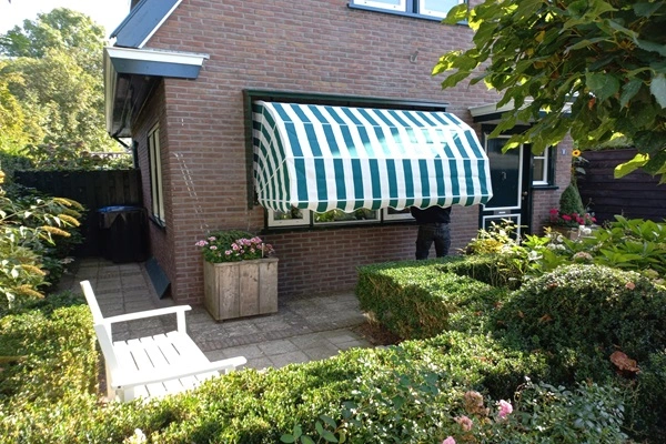 Groen-wit gestreepte markies voor raam in tuin van bakstenen huis Groen-wit gestreepte markies voor raam in tuin van bakstenen huis