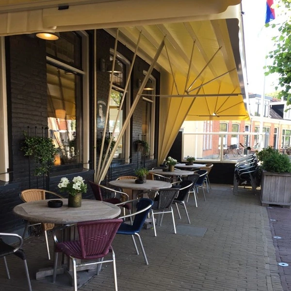 Horeca markies bij cafe met geel zonnescherm en terrastafels met stoelen