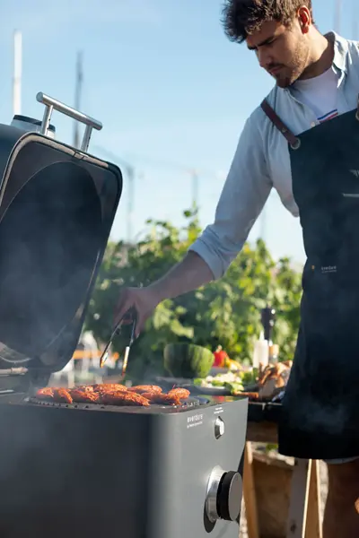 Man bij houtskool BBQ Everdure 4K met gegrilde kip Man bij houtskool BBQ Everdure 4K met gegrilde kip