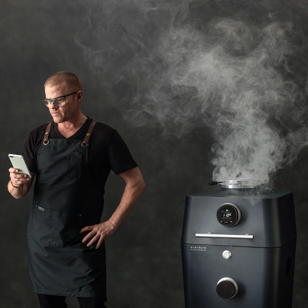 Man met telefoon naast Everdure BBQ vol rook