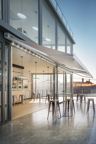 Nodo knikarmscherm bij glazen gevel van restaurant met barkrukken buiten Nodo knikarmscherm bij glazen gevel van restaurant met barkrukken buiten