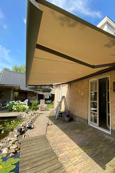 Opal zonnescherm boven terras met klinkers naast vijver en openslaande deuren Opal zonnescherm boven terras met klinkers naast vijver en openslaande deuren