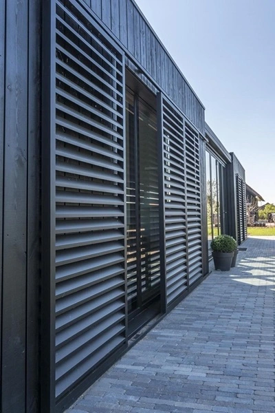 Schuifluiken bij glazen schuifdeur van een zwart houten huis met grijze bestrating Schuifluiken bij glazen schuifdeur van een zwart houten huis met grijze bestrating