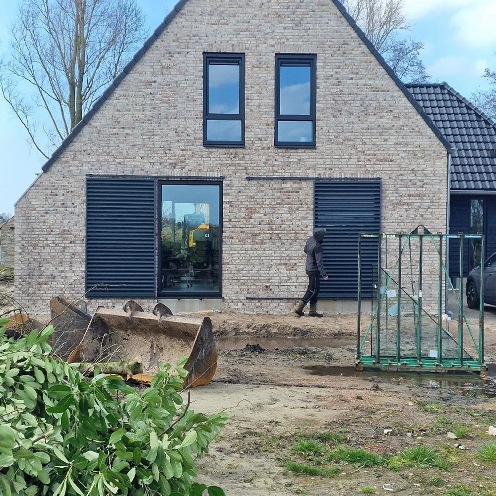 Schuifluiken zonwering geïnstalleerd op een bakstenen huis met zwarte dakbedekking