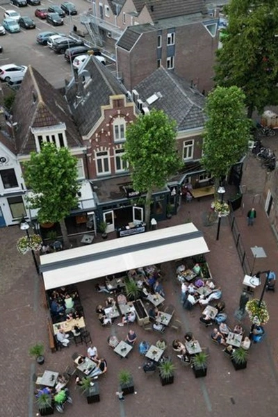 Zon en regenwering horeca terras met mensen onder luifel naast kerk Zon en regenwering horeca terras met mensen onder luifel naast kerk