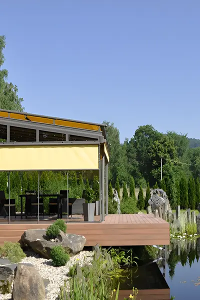 Glazen tuinkamer Terrazza Sempra met zonwering naast vijver en tuin Glazen tuinkamer Terrazza Sempra met zonwering naast vijver en tuin