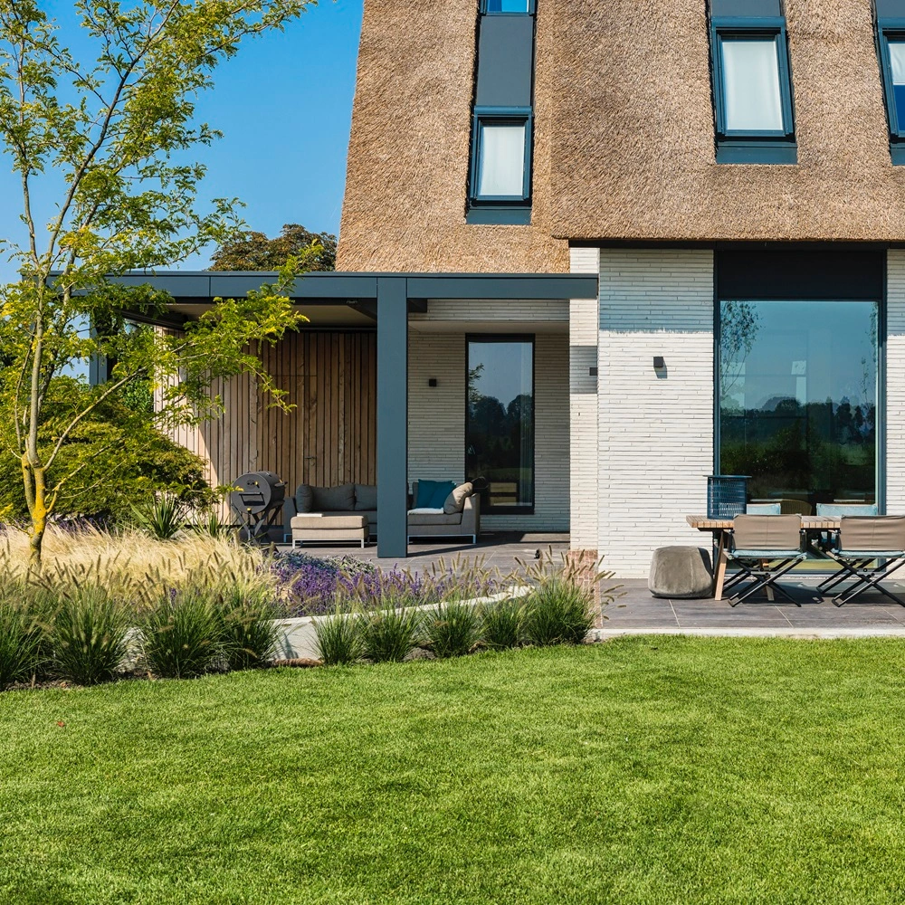 Zenit tuinkamer met schuifdak en tuinset aan moderne villa met rieten dak