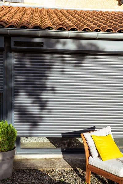 Zwart solar rolluik met terrasstoel en geel kussen op de voorgrond Zwart solar rolluik met terrasstoel en geel kussen op de voorgrond