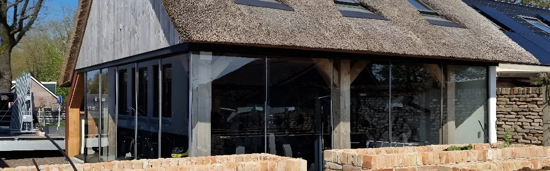 Glazen schuifwanden in een buitenverblijf met rieten dak en bakstenen details Glazen schuifwanden in een buitenverblijf met rieten dak en bakstenen details