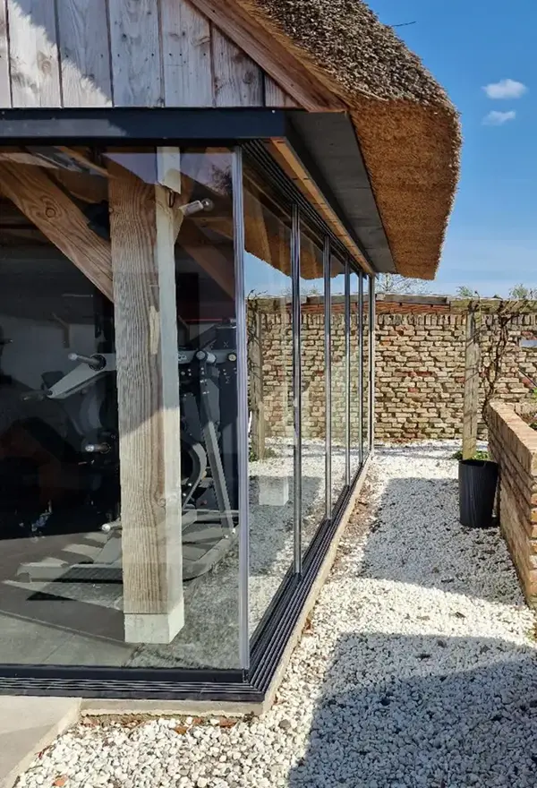 Glazen schuifwanden met houten steunpalen in buitenverblijf Glazen schuifwanden met houten steunpalen in buitenverblijf