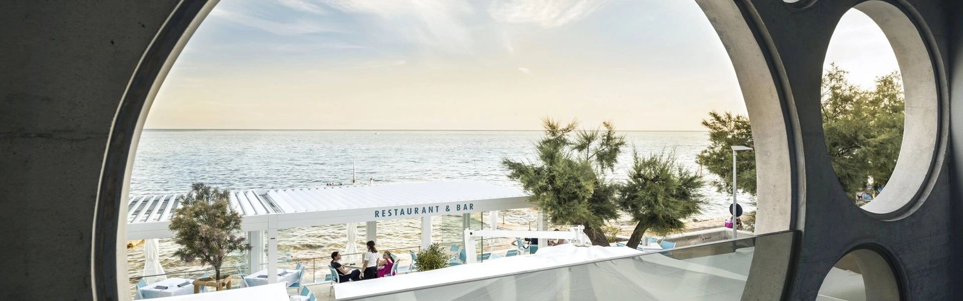 Hotelterras met overkapping en uitzicht op zee door ronde ramen