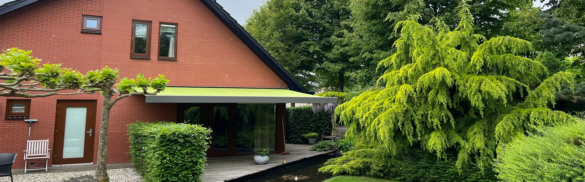Knikarmscherm aan huis met groene tuin en vijver Knikarmscherm aan huis met groene tuin en vijver