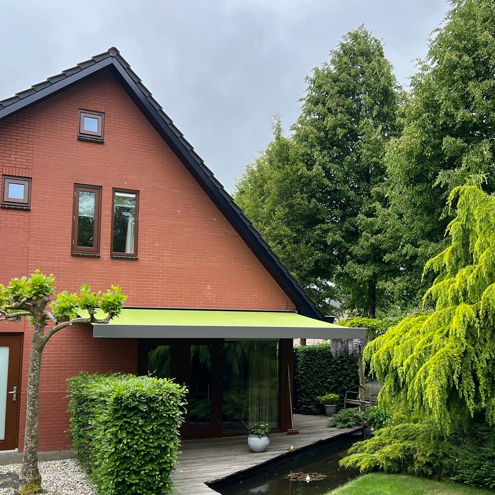 Knikarmscherm aan rood huis met tuin en vijver Knikarmscherm aan rood huis met tuin en vijver