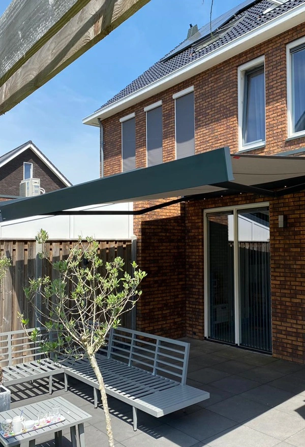 Knikarmscherm boven terras met zithoek en houten schutting Knikarmscherm boven terras met zithoek en houten schutting