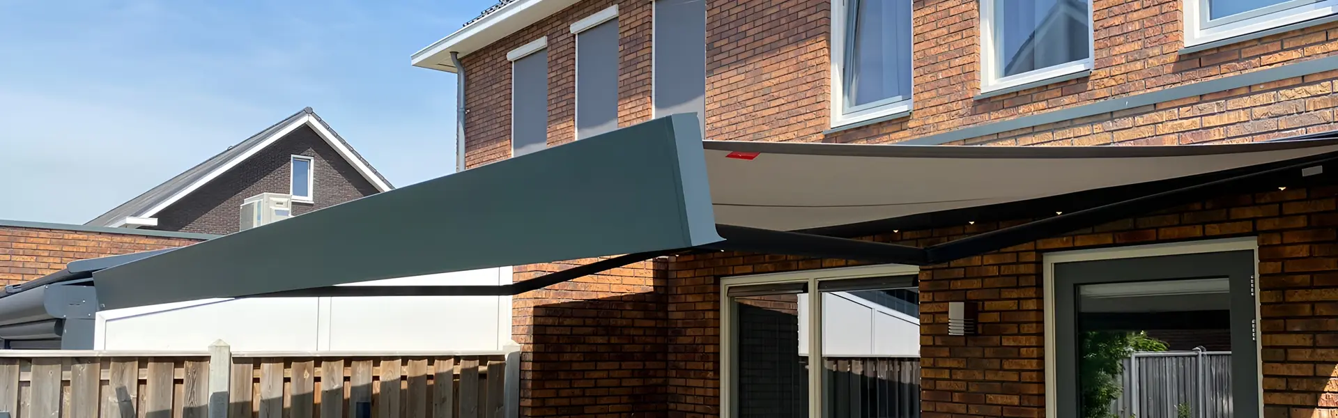 Knikarmscherm boven terras naast raam en schutting Knikarmscherm boven terras naast raam en schutting