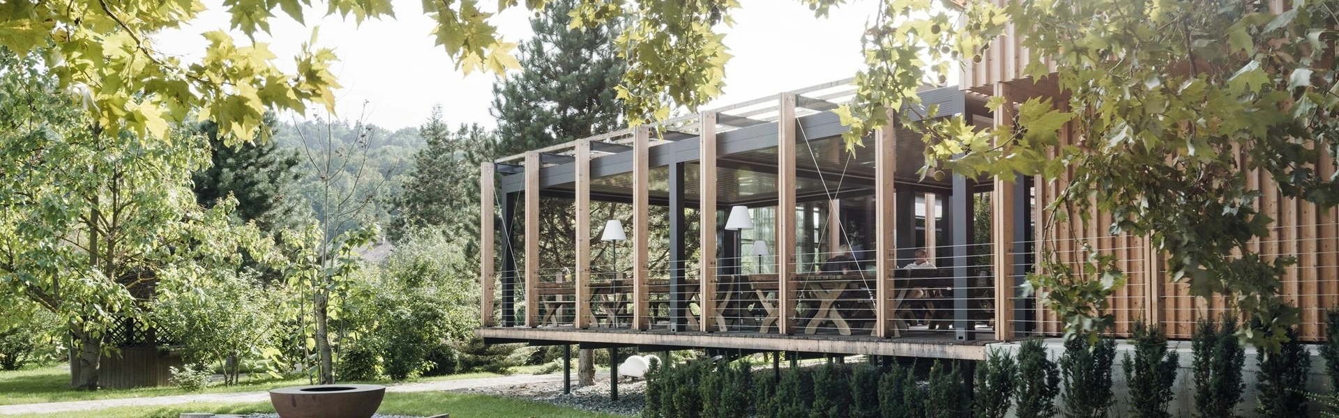 Overkapping met houten frame en glazen panelen, omringd door groen