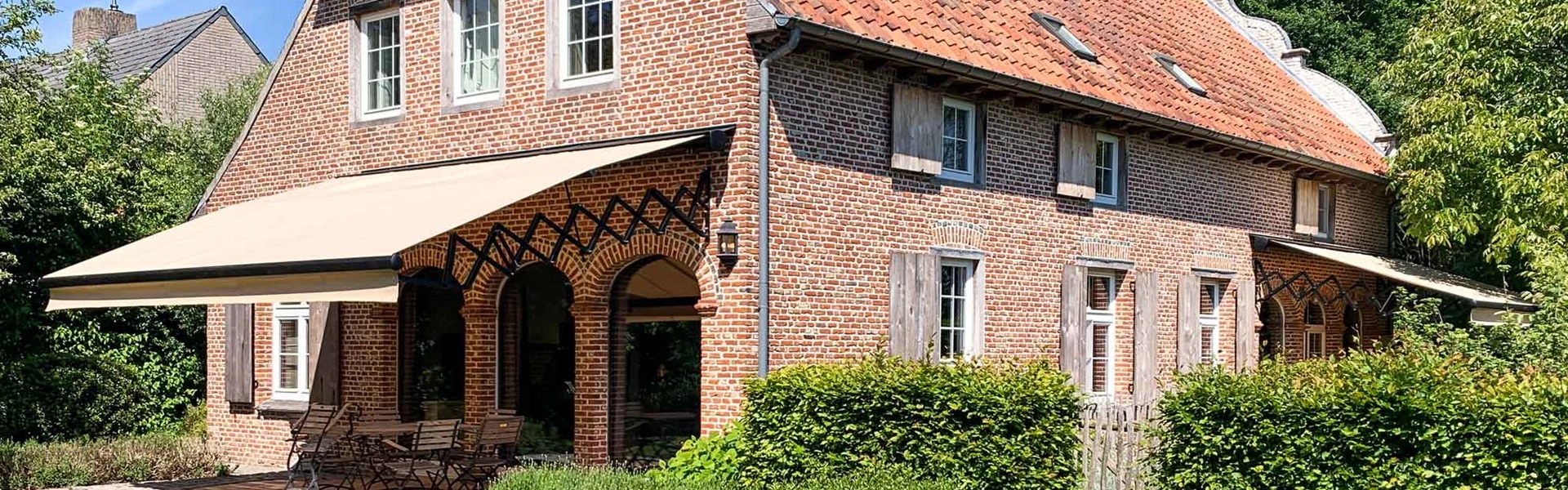 Schaararmscherm aan de gevel van een huis biedt zonwering voor het terras