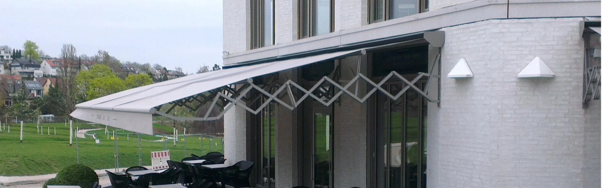 Schaararmscherm boven terras met zwarte stoelen bij modern gebouw