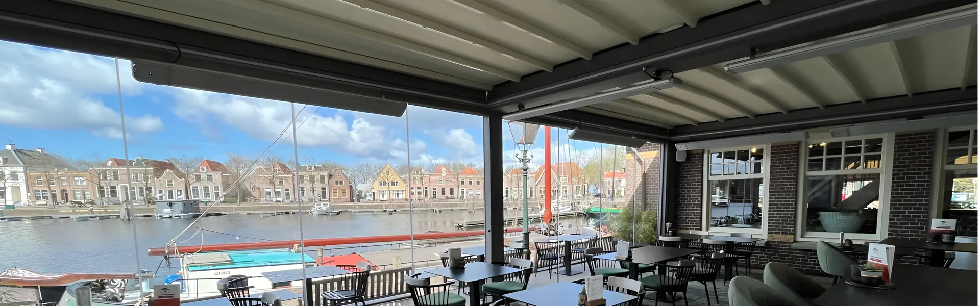 Terrasoverkapping met schuifdak en glazen panelen bij een restaurant met uitzicht op een haven