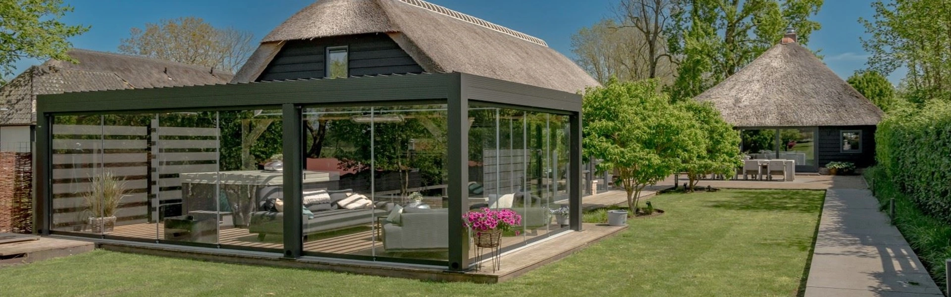 Tuinkamer met glazen wanden in landelijke tuin met rieten dak en groen uitzicht