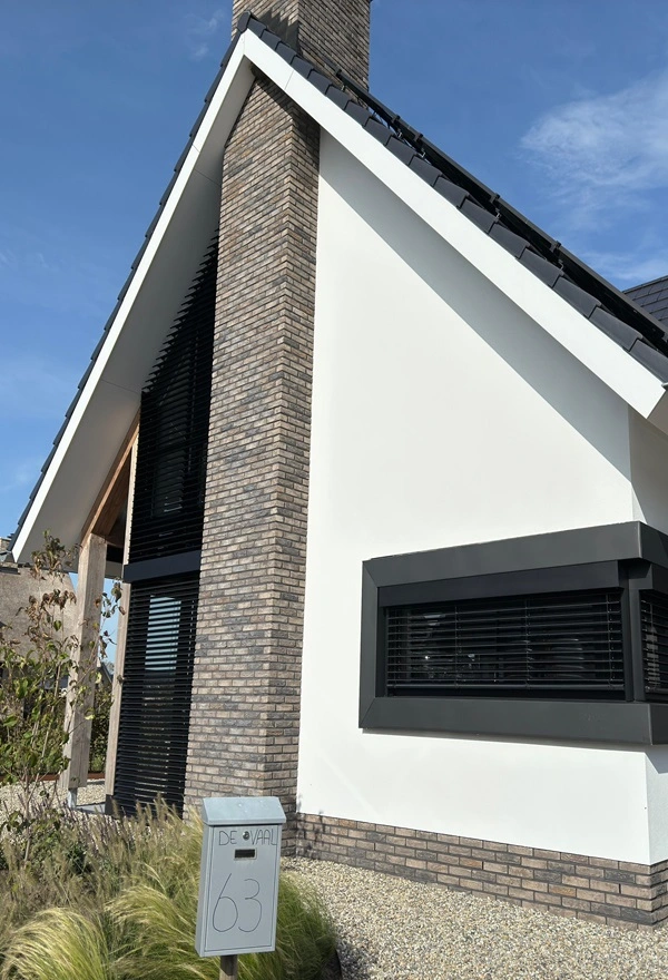 Woning met schuine gevel en zwart-witte buitenjaloezieen naast een grote schoorsteen Woning met schuine gevel en zwart-witte buitenjaloezieen naast een grote schoorsteen