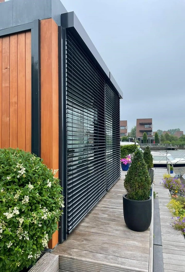Zwarte buitenjaloezieen met houten gevelbekleding en groene planten op een terras Zwarte buitenjaloezieen met houten gevelbekleding en groene planten op een terras