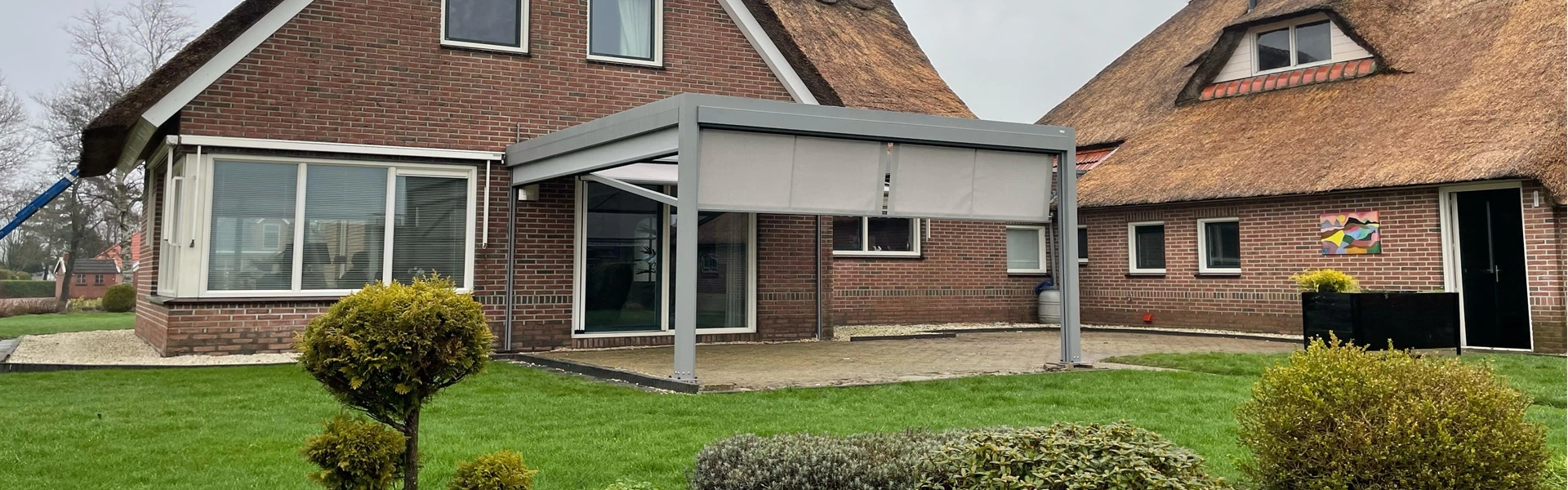Aluminium overkapping Qbus naast rietgedekte woning in landelijke tuin