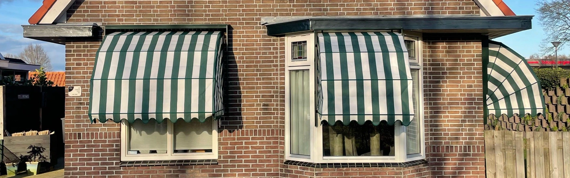 Bakstenen woning met groen-wit gestreepte houten markiezen en een rode dakpan
