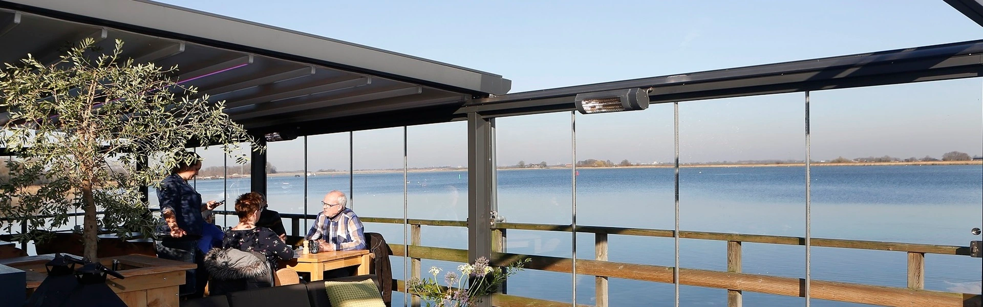 Binnenzicht van een terras met glazenschuifwanden en uitzicht op het meer