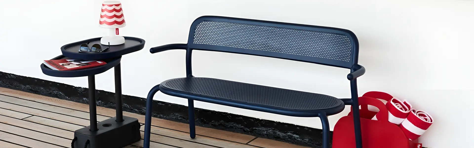 Blauw outdoor bankje met bijzettafel en rode accessoires op een houten terras