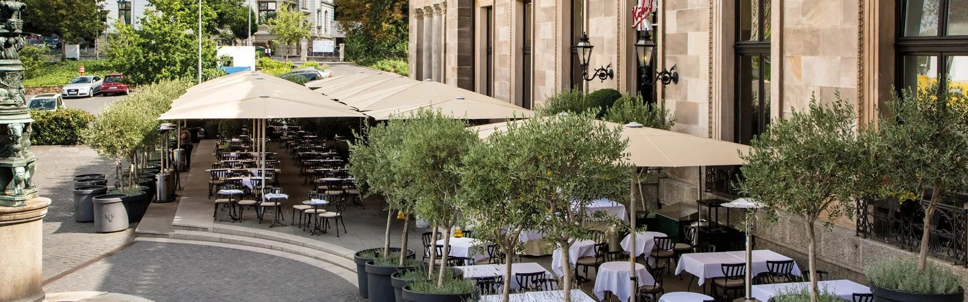Cremekleurige Schatello-parasols op een klassiek terras met tafels en stoelen