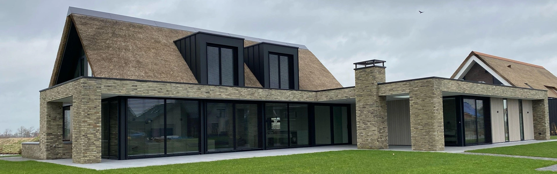 Eigentijdse woning met rieten dak en strakke buitenjaloezieën voor privacy en schaduw