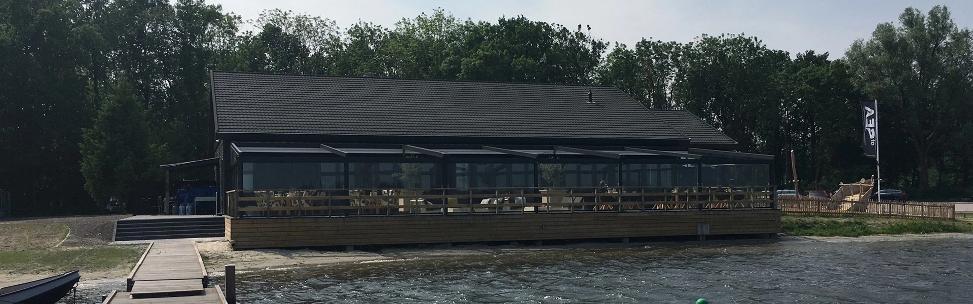 Exterieur van een gebouw met terrasoverkapping en glazenschuifwanden langs de oever