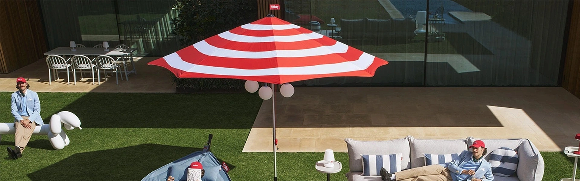 Fatboy parasol met rood witte strepen in een tuin met loungeset en hangmat