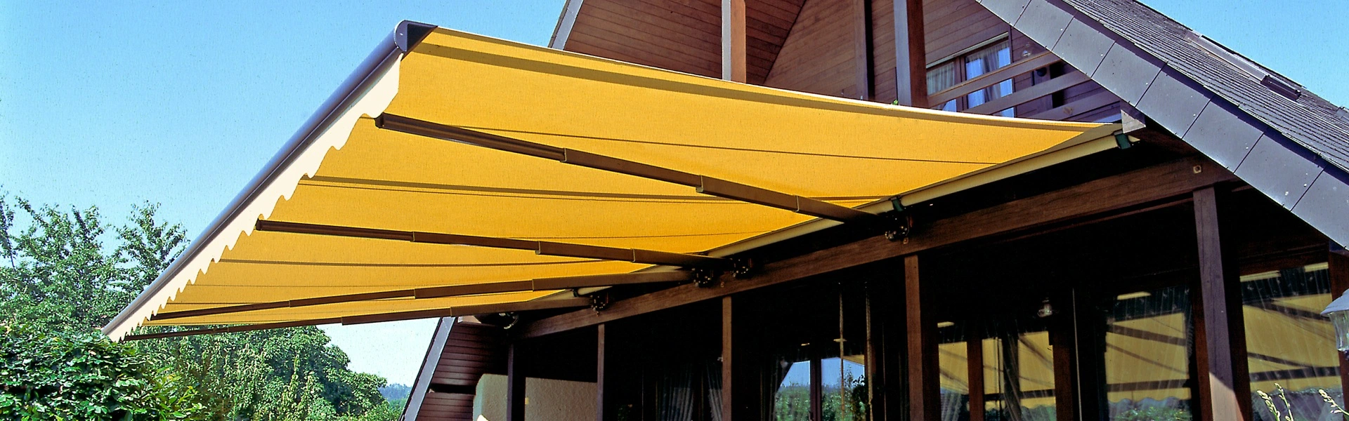 Geel knikarmscherm Jumbo boven terras van houten woning