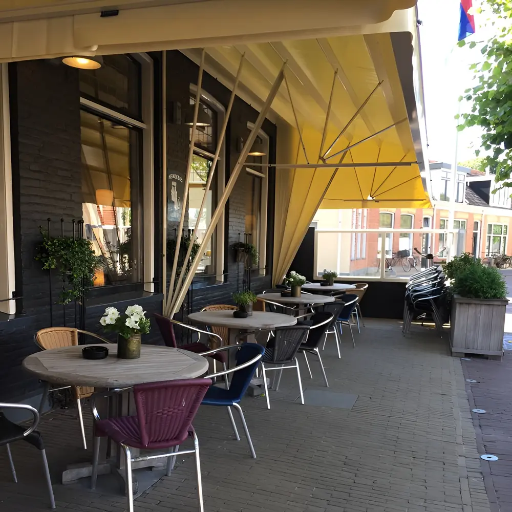 Gele aluminium markies boven terras met houten tafels bij Cafe Nap