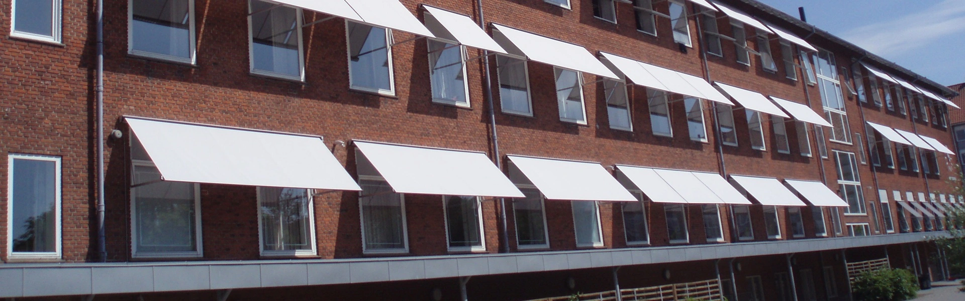 Gevel met meerdere witte uitvalschermen op een bakstenen gebouw