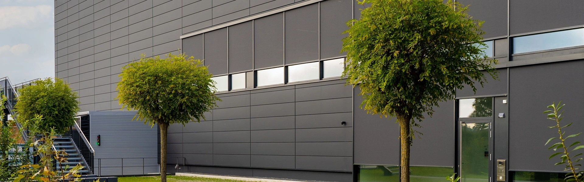 Grijze Roma zipscreen F50 op zakelijke gevel met groene bomen