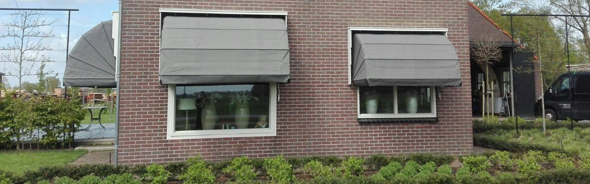 Grijze markiezen boven terrasdeuren van een bakstenen huis met tuinmeubilair